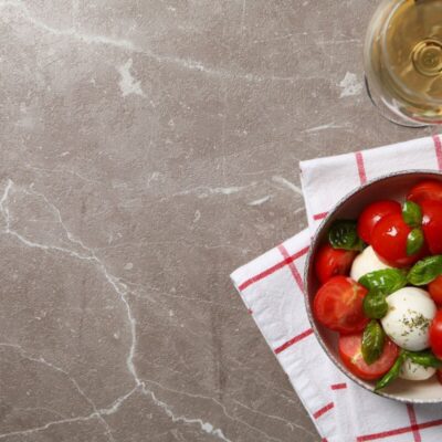 Sałatka caprese i kieliszek wina na marmurowym blacie kuchennym.