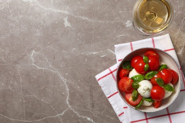 Sałatka caprese i kieliszek wina na marmurowym blacie kuchennym.